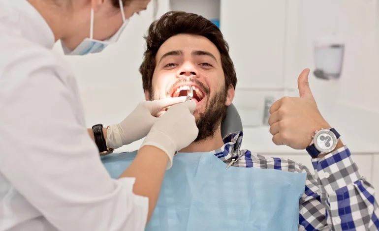 Smiling man sits in dentist chair, giving thumbs up gesture for positive experience.