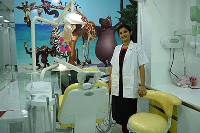 A dentist stands next to a chair in a children's dental clinic with cartoon pictures on the wall.