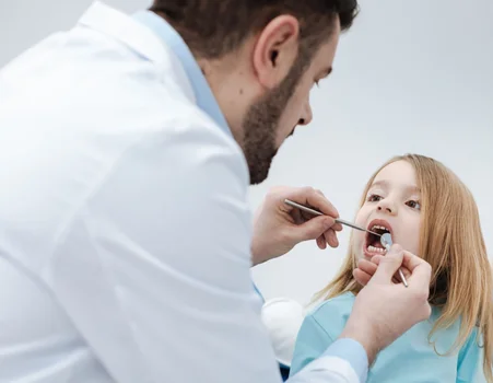 A youngster is receiving her dentures inspected by a dental professional while seated in the chair.